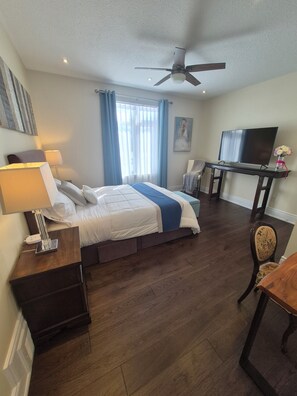 A hotel room with a bed, a desk with a TV, a chair, and a ceiling fan. - Romantic Lakeside Cozy Queen Suite Free Breakfast (Niagara Falls)