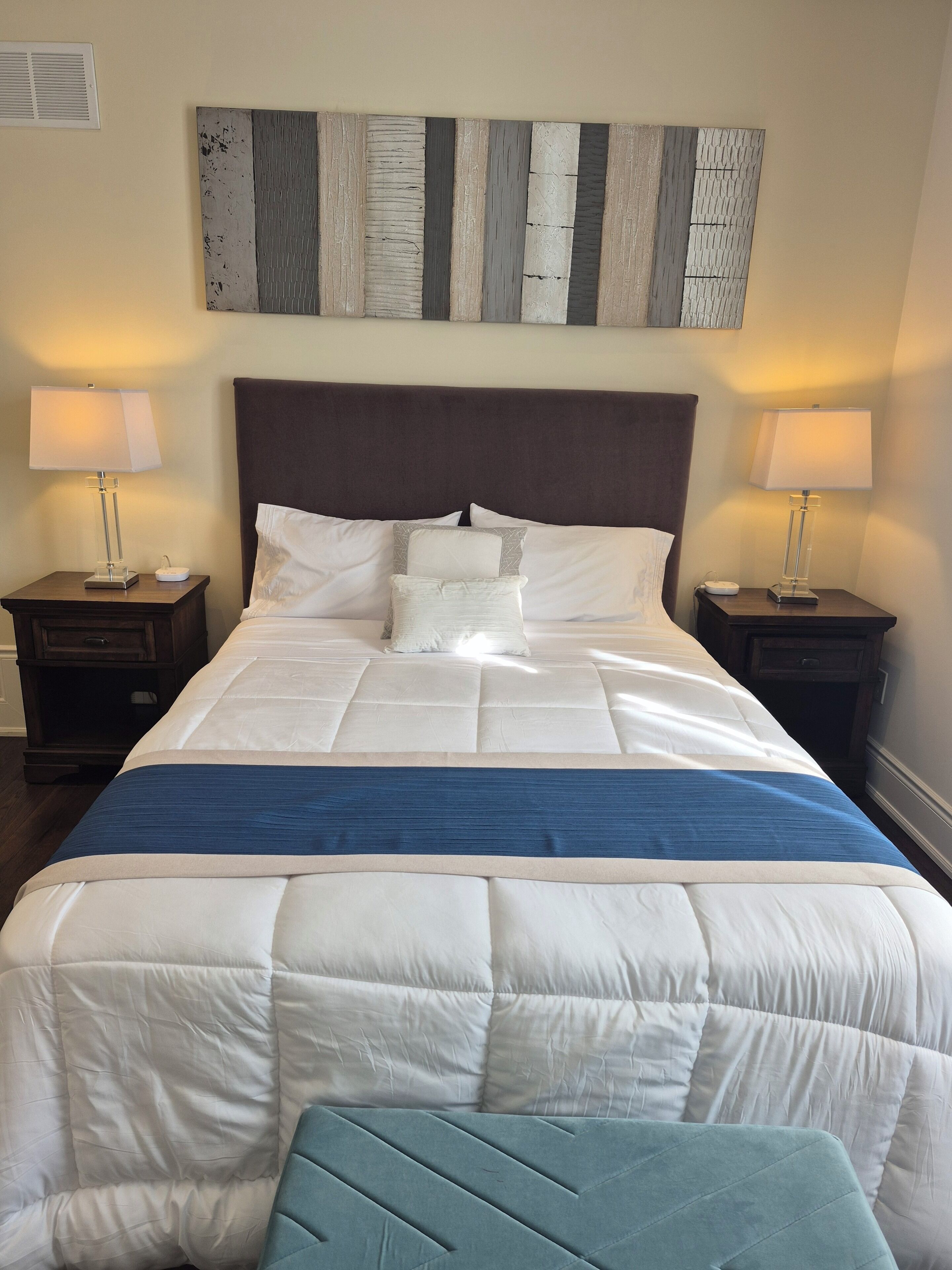 A neatly made bed with white and blue bedding, two bedside tables with lamps, and a wall art piece above the bed.
