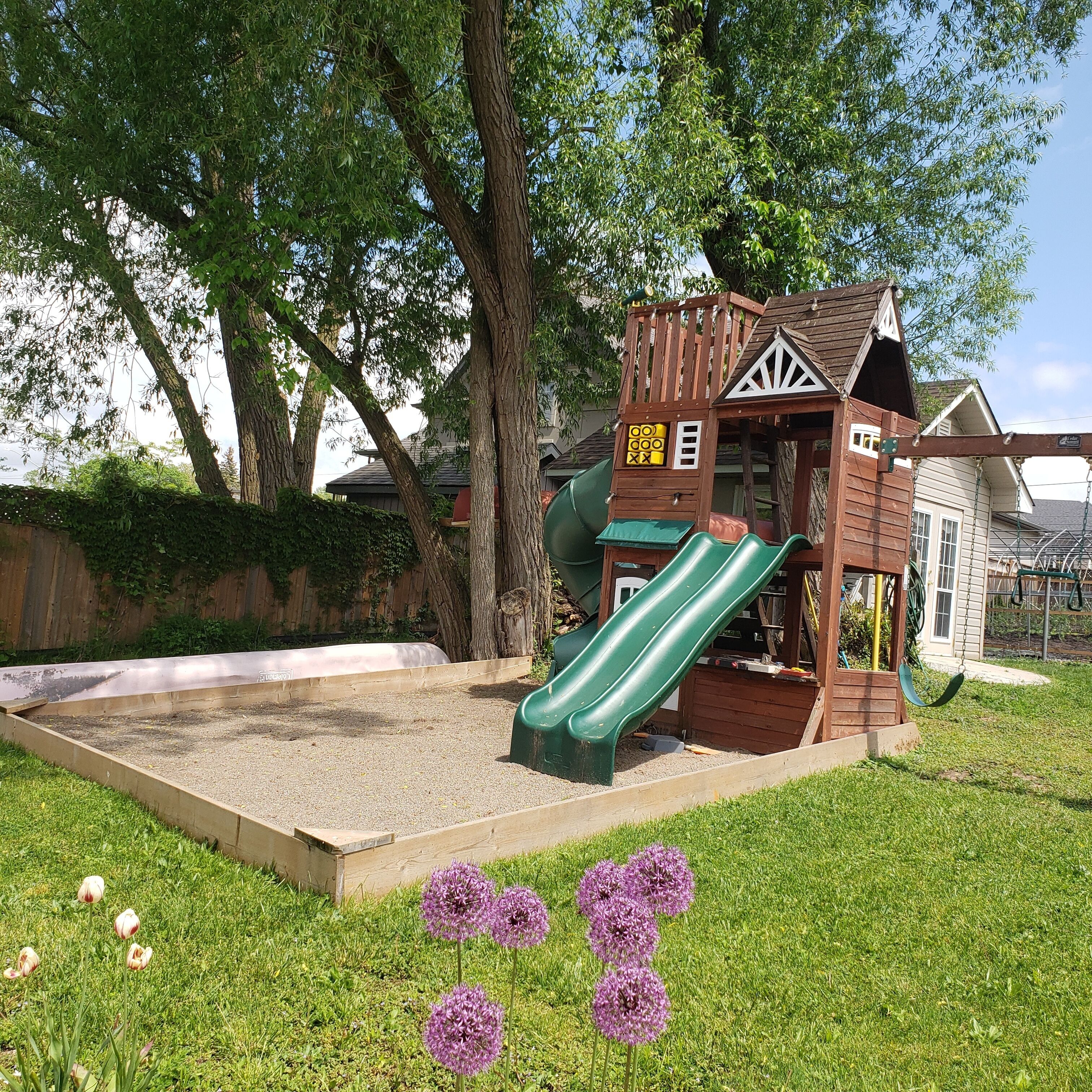 A playground with a slide and climbing structures, surrounded by grass and trees.
