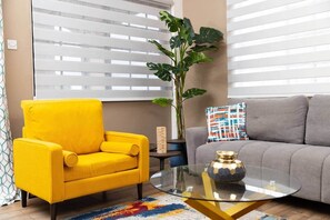 A living room with a yellow armchair, a grey sofa, a glass coffee table, and a large plant. - Ahra Suites come for the views (Ground Floor) (Arnos Vale)