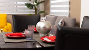 Une table à manger dressée avec des assiettes rouges, des verres transparents et un saladier en argent.