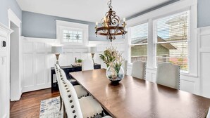 A dining area with a wooden table, white chairs, a chandelier, and a window with blinds. - Historic Home with King Bed (High Point)