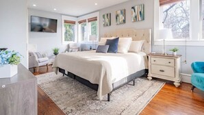 A bedroom with a large bed, bedside tables, a TV, and a window with blinds. - Historic Home with King Bed (High Point)