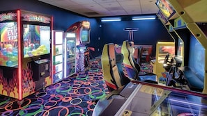 Une salle avec des jeux d’arcade, une moquette colorée et un panneau lumineux au néon.