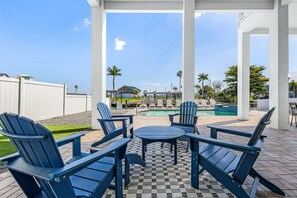 Ein überdachter Sitzbereich im Freien mit Adirondack-Stühlen und einem Tisch, mit Blick auf einen Pool und das Meer.