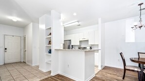 A modern kitchen with white cabinets, a central island, and a dining area with a wooden table and chairs.