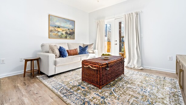 A living room with a white sofa, a wooden coffee table, a wicker chest, and a patterned rug.