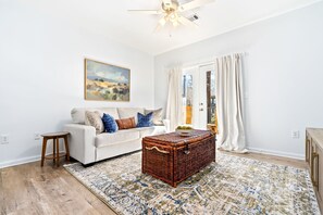 A living room with a white sofa, a wooden coffee table, a wicker chest, and a patterned rug. - New Modern Getaway ~ 1br, Patio & Pool (Auburn)