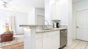 A kitchen with white cabinets, a granite countertop, a stainless steel dishwasher, and a ceiling fan.