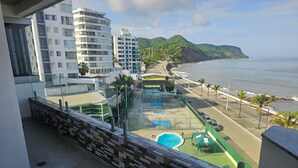 A view of a hotel with a pool area, a beach, and a mountainous backdrop.