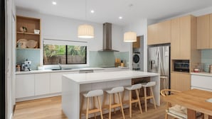 A modern kitchen with a central island, bar stools, a built-in oven, and a large window. - The Cape House in Cape Woolamai (Cape Woolamai)