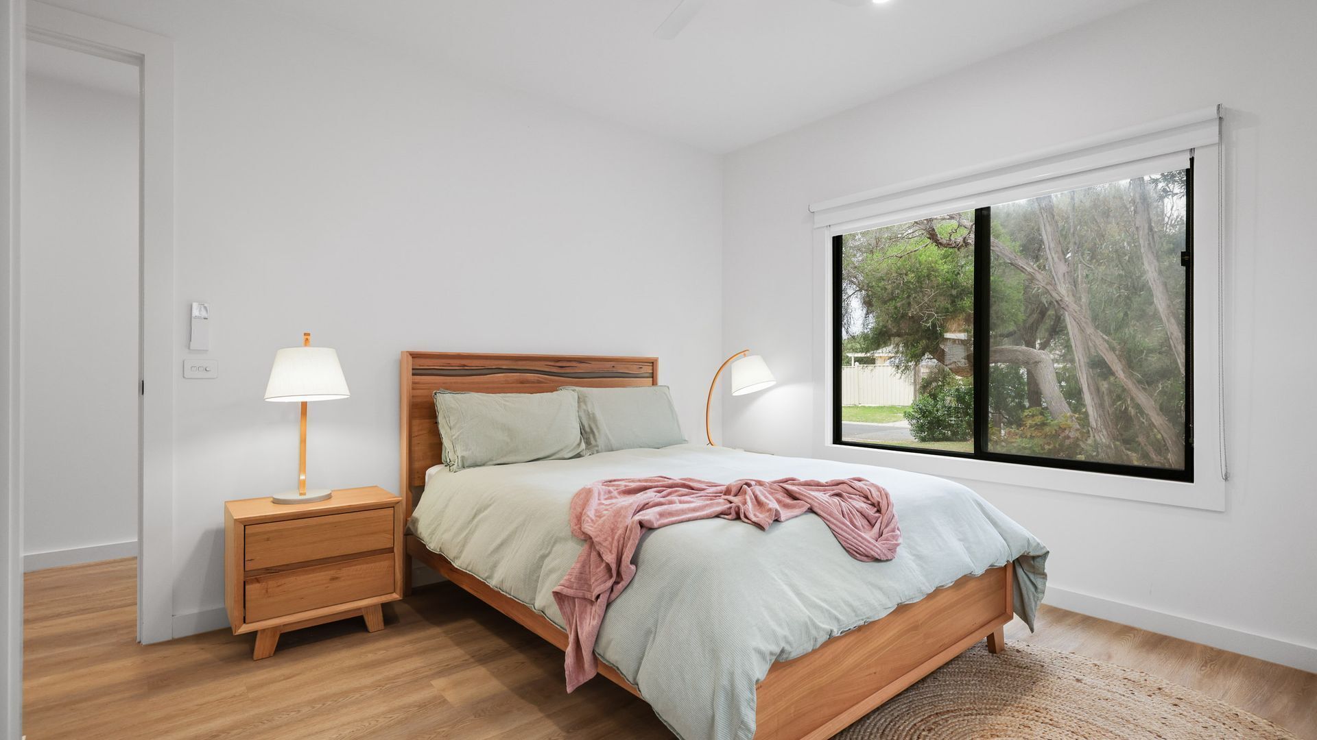 Un dormitorio con una cama de madera, mesitas de noche y un ventanal con vistas a árboles.