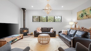 A modern living room with a fireplace, leather sofas, a TV, and a large window. - The Cape House in Cape Woolamai (Cape Woolamai)