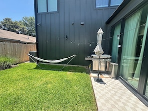 Ein Garten mit einer Hängematte, einem Grill und einer Terrasse.