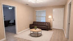 A living room with a brown leather sofa, a round coffee table with a plant, a lamp, and a door. - Spacious 4BR Norco Retreat; Near SilverLakes; Pet Friendly; RV Parking (Norco)