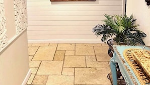 Un pasillo con un cuadro de una escena de playa, una planta en maceta y una mesa con camino de mesa tejido.