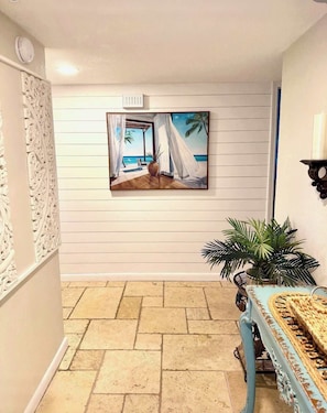 A room with a beach-themed painting, a potted plant, and a table with a woven table runner. - Seascape Villa: Beach Access, Pools, Golf, Music (Miramar Beach)