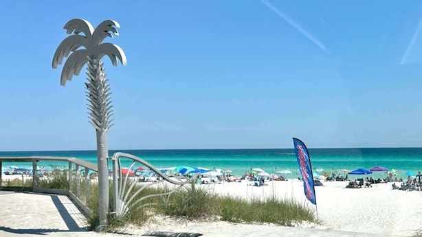 Una playa con una escultura de palmera, una bandera y un cielo azul despejado.