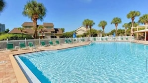 Una piscina con borde de baldosas, rodeada de palmeras y una valla.