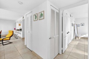 A modern, well-lit room with white walls, a yellow chair, a dining table, and a kitchen area in the background. - Brickell City Centre Condo with Pool & Parking (Miami)