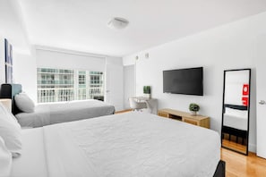 Ein modernes Hotelzimmer mit zwei Betten, einem Fernseher, einem Schreibtisch und einem großen Fenster.