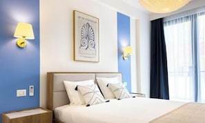 Una habitació d'hotel amb un llit gran, dues taules de nit, una obra d'art penjada a la paret i una finestra amb cortines.
