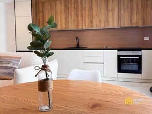 A modern kitchen with wooden cabinets, a built-in oven, and a dining table with a glass vase. - "Blue" – Adults Only (+16) (Sarandë)