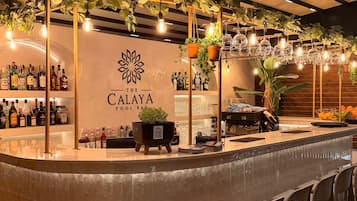 Zona de bar con mostrador, taburetes, plantas colgantes y un letrero que dice 'The Calaya Pool Bar'.