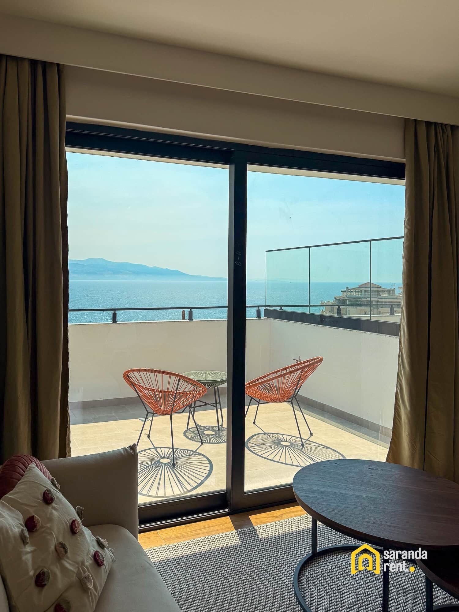 Un balcón con vista al mar, con dos sillas de mimbre y una mesita.