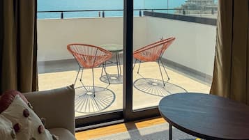 Un balcón con vista al mar, con dos sillas de mimbre y una mesita.