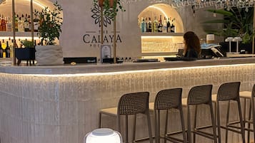 Zona de bar con mostrador, sillas, una mesa con lámpara y un letrero que dice 'The Calaya'.