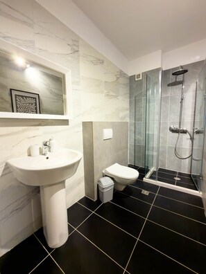 Ein Badezimmer mit Marmorwand, Waschbecken, Toilette und einer Duschkabine.