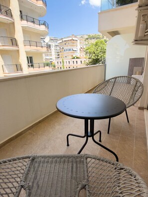 Ein Balkon mit rundem Tisch und zwei Korbstühlen, mit Blick auf ein Wohngebiet mit mehrstöckigen Gebäuden.