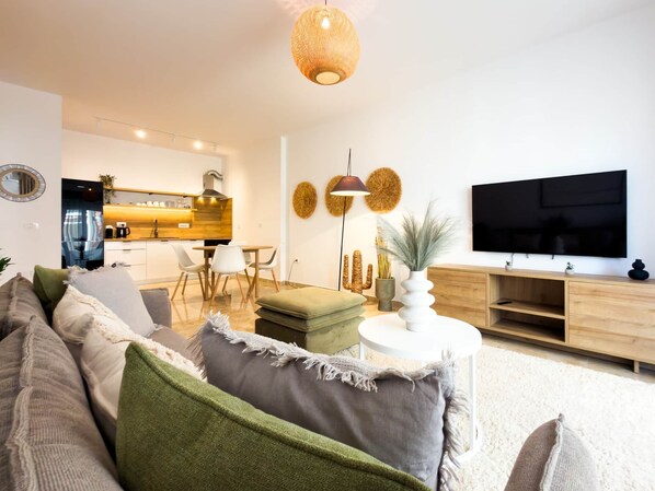 Ein modernes Wohnzimmer mit Sofa, Couchtisch, Fernseher und einer Küche im Hintergrund.