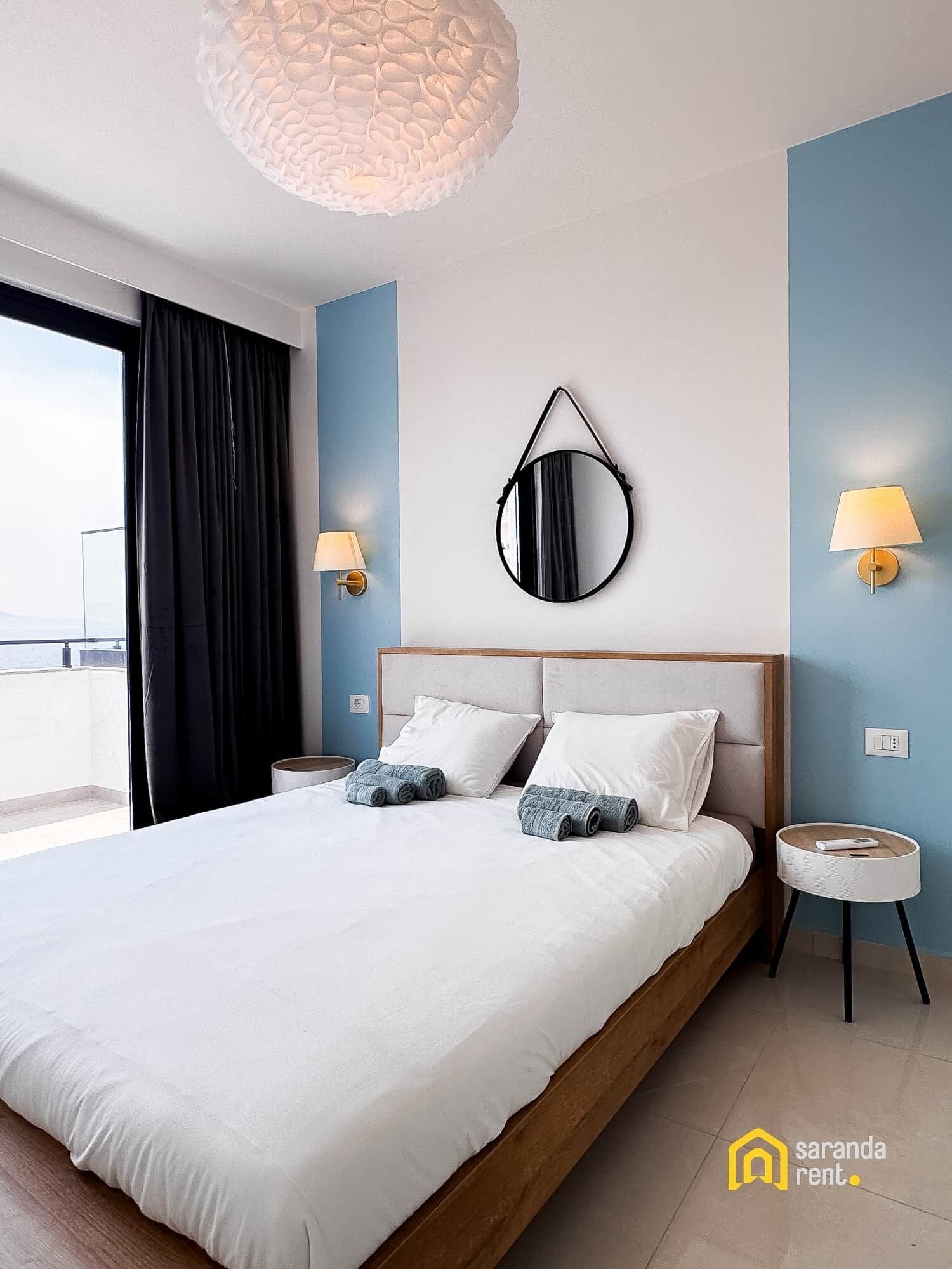 Een moderne slaapkamer met een groot bed, een ronde spiegel, twee bedlampjes en uitzicht op de omgeving.