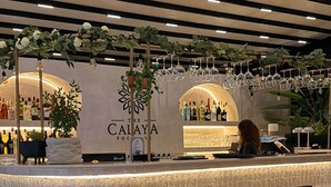Een bar met een toonbank, stoelen, een tafel met een lamp, en een bord waarop 'The Calaya' staat.