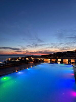 Una piscina en la azotea con vistas al mar y al paisaje urbano al atardecer.