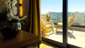 Een balkon met rieten stoelen, een tafel met een bloevas, en uitzicht op de skyline.