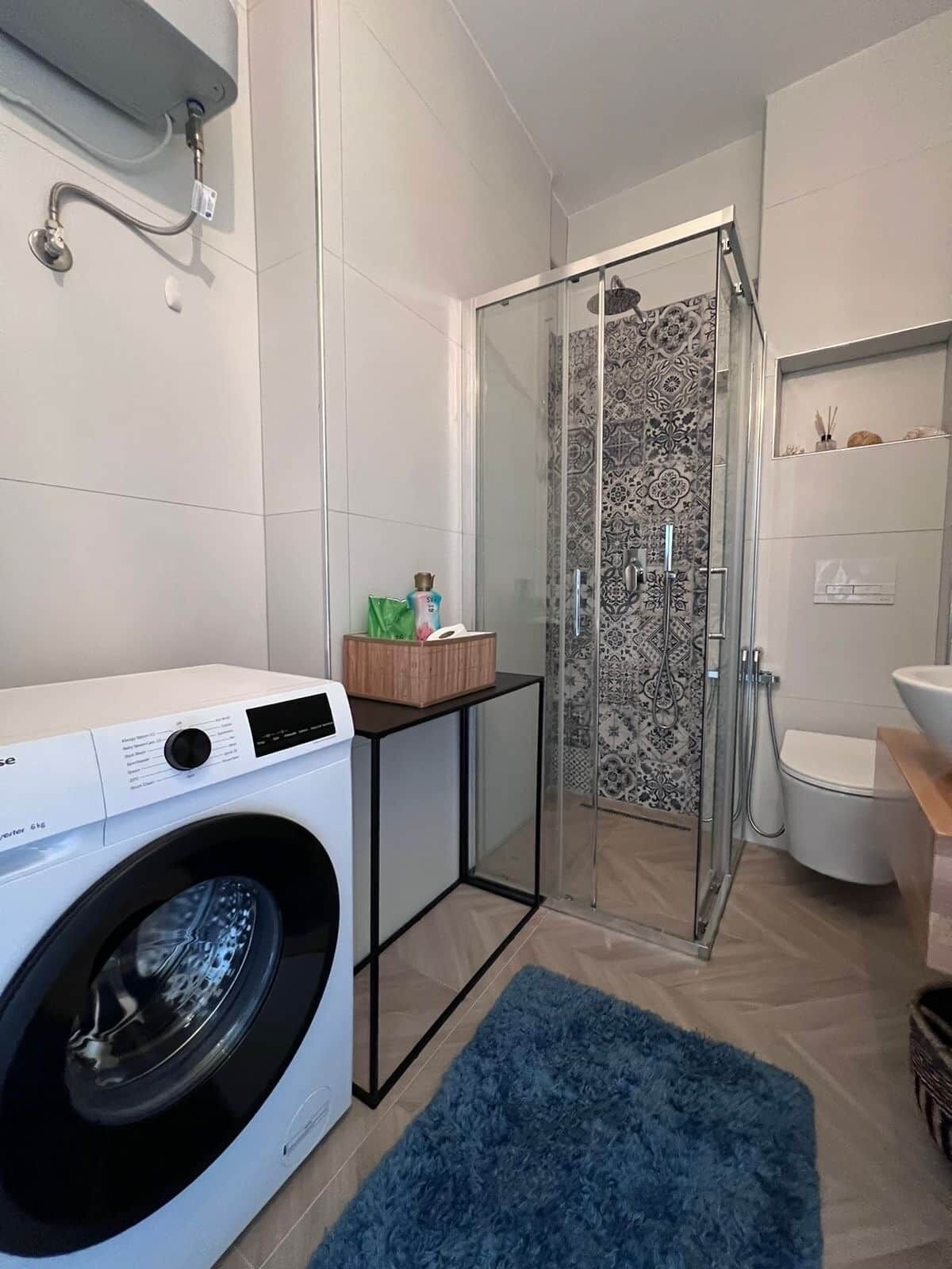 Een compacte, moderne badkamer met een douchecabine van glas, een ingebouwde wasmachine en een toilet.