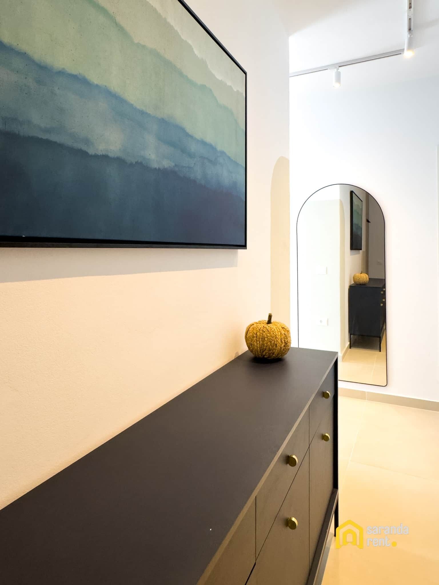 A modern interior with a large abstract painting, a dark console table, and a decorative pumpkin.