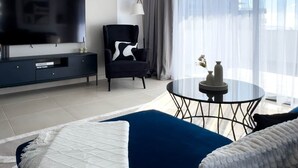 Ein modernes Wohnzimmer mit Fernseher, einem schwarzen Sessel, einem runden Glastisch und einem blauen Sofa.