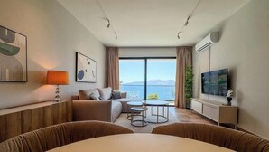 Camera d'albergo moderna con divano, due tavolini, televisione e un'ampia finestra vista mare.