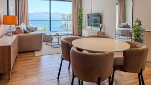 Una moderna camera d'albergo con un tavolo rotondo, sedute confortevoli, una TV a schermo piatto e una grande finestra vista mare.
