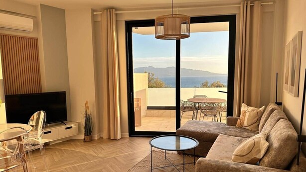 A modern living room with a sofa, TV, and clear glass table. - Valentina - Corfu View Residence (Sarandë)
