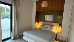 A modern bedroom with a large bed, a wooden headboard, and a view through a sliding door. - Valentina - Corfu View Residence (Sarandë)