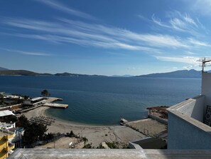 Blick auf die Küste mit blauem Himmel, ruhiger See und fernen Bergen.