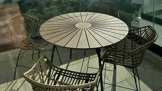 Un balcone con un tavolo rotondo e sedie in vimini che si affaccia su una vista costiera.