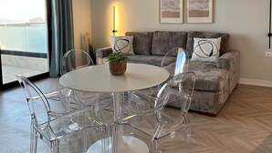 A modern living room with a round white table, clear chairs, a grey sofa, and two framed pictures on the wall. - Valerie - Corfu View Residence (Sarandë)