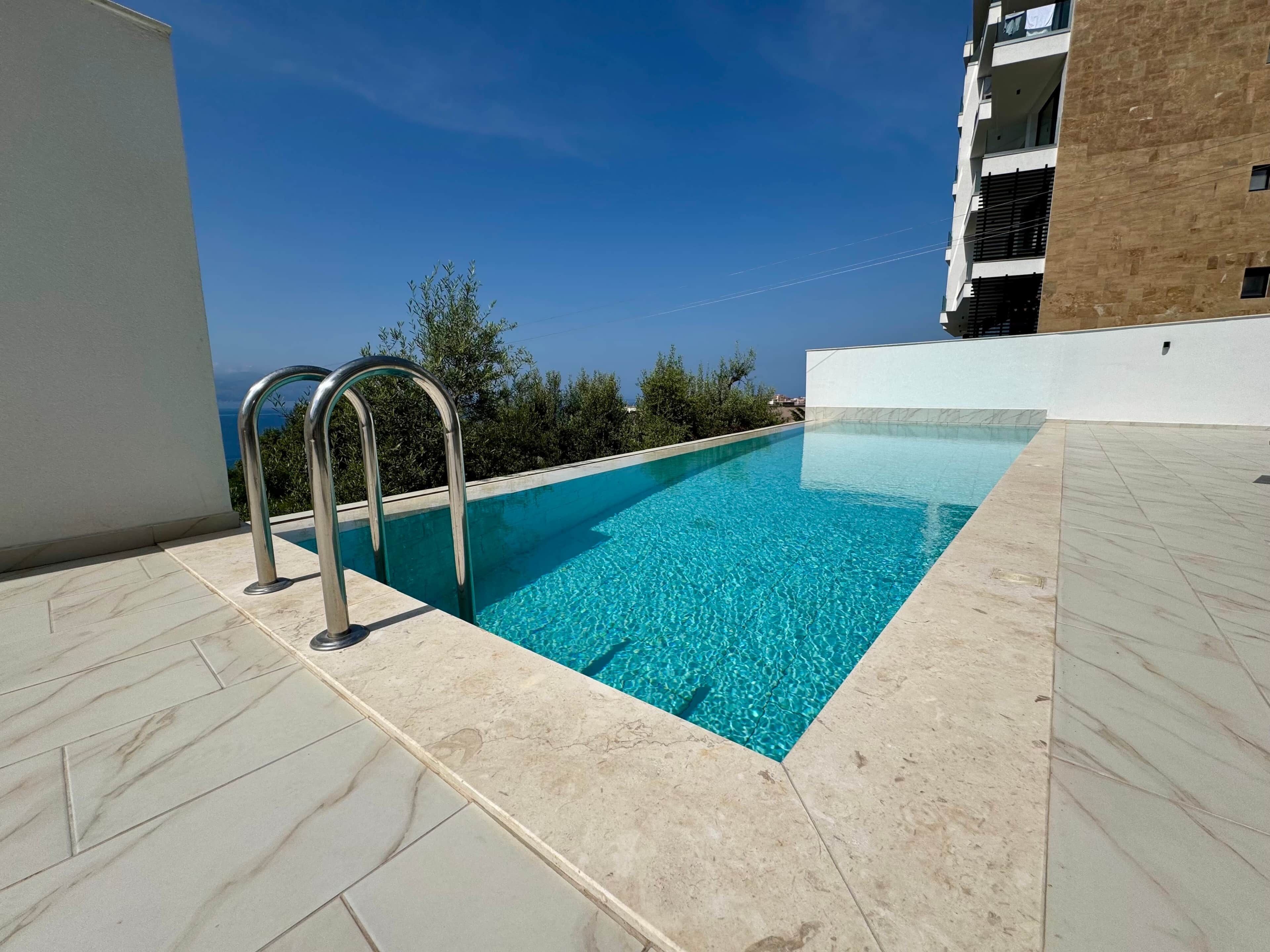 Ein rechteckiger Swimmingpool mit klarem, blauem Wasser, umgeben von hell gefliestem Boden.