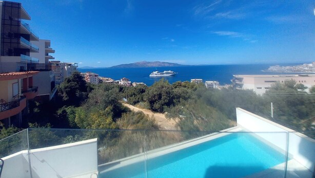 A balcony with a clear view of the sea, a swimming pool, and surrounding buildings. - Valerie - Corfu View Residence (Sarandë)